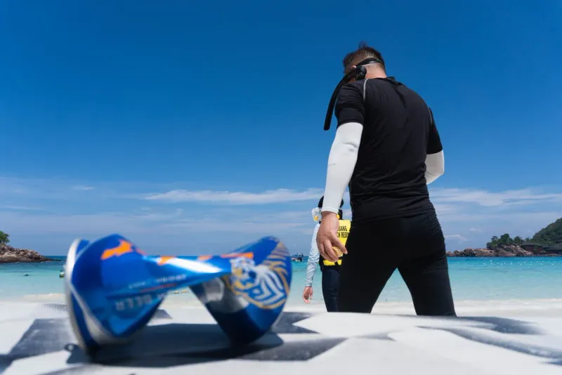 Volunteer walking towards the ocean with snorkeling gear for a reef survey on Koh Samui