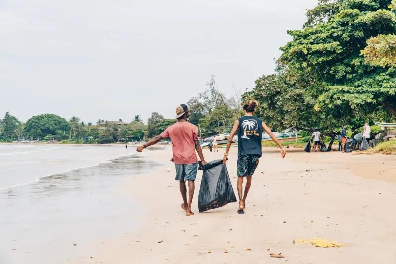 Volunteers carrying trash bags along a beach shoreline during a community cleanup