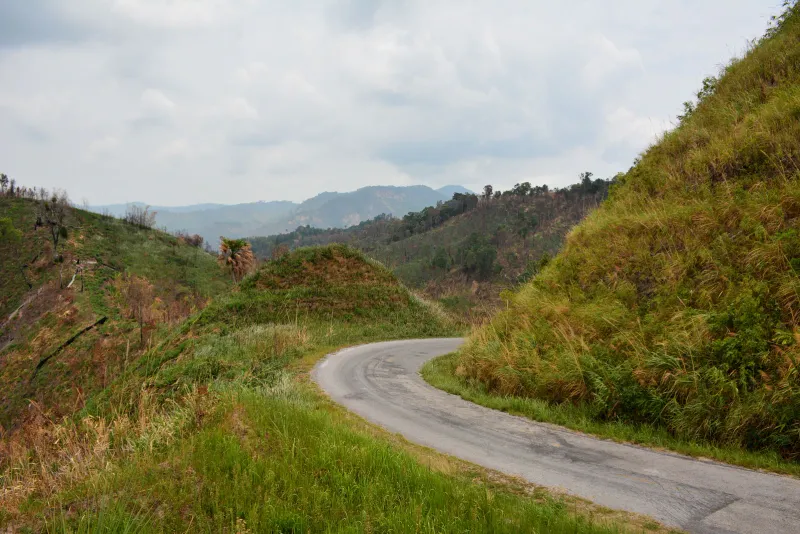 Winding narrow tarmac road climbing through grassy hills in Thailand