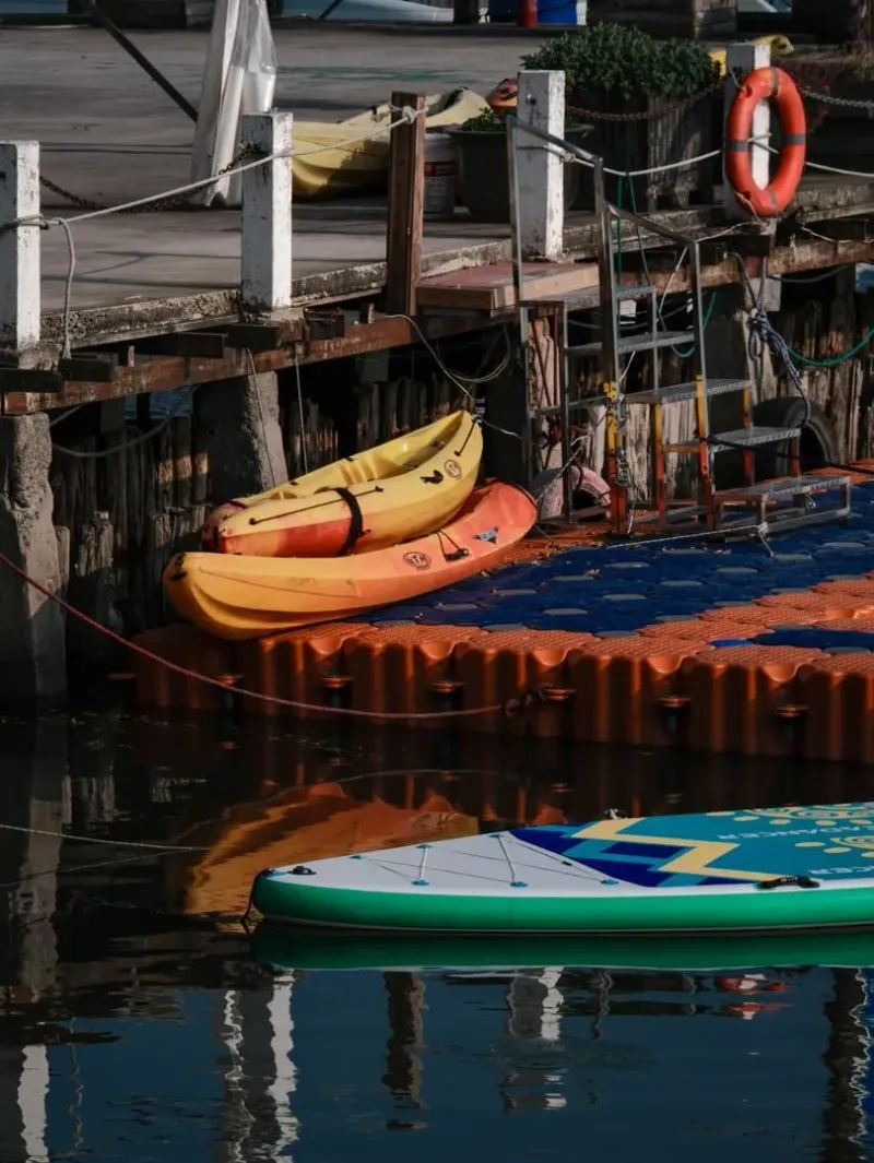 Colorful kayaks and a paddleboard moored along a rustic wooden harbor dock