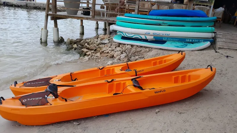 Bright orange kayaks resting on a sandy tropical beach next to stacked paddleboards