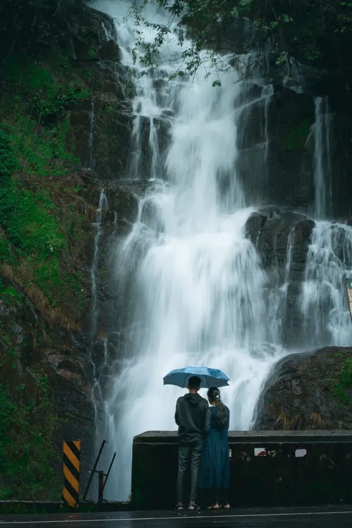 A waterfall in full flow after rain, a walker with an umbrella below