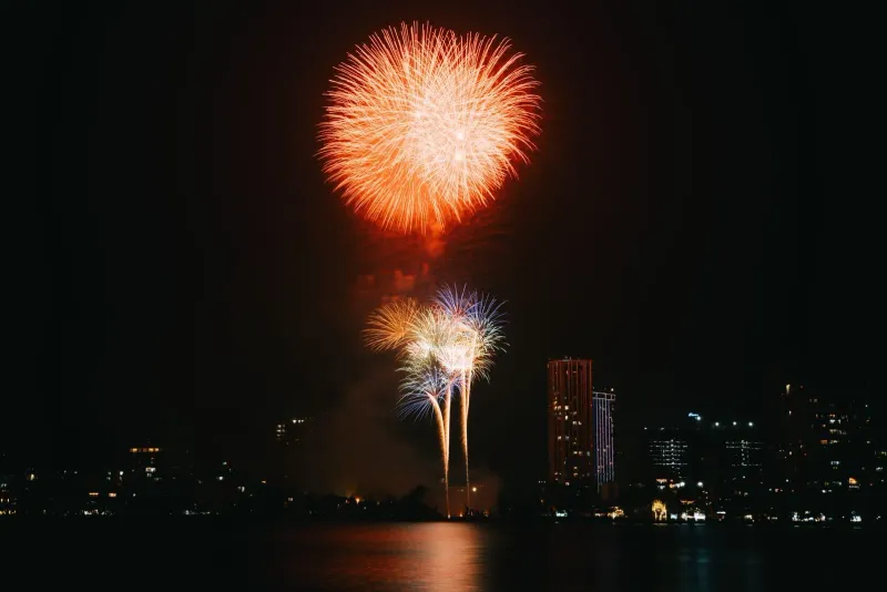 Fireworks reflecting off calm water near a beachfront skyline during a Koh Samui New Year celebration