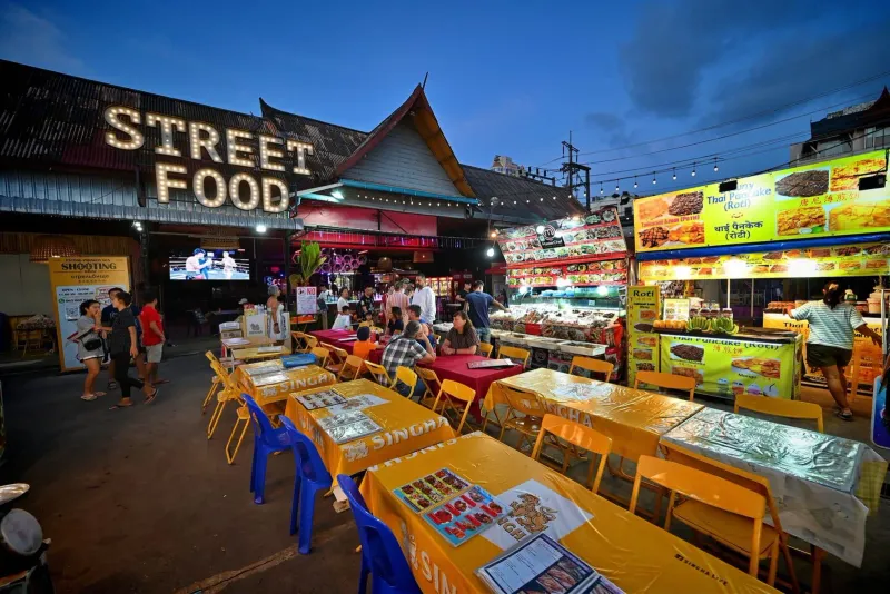Colorful street food stalls lit up at a Thai night market with vendors serving customers