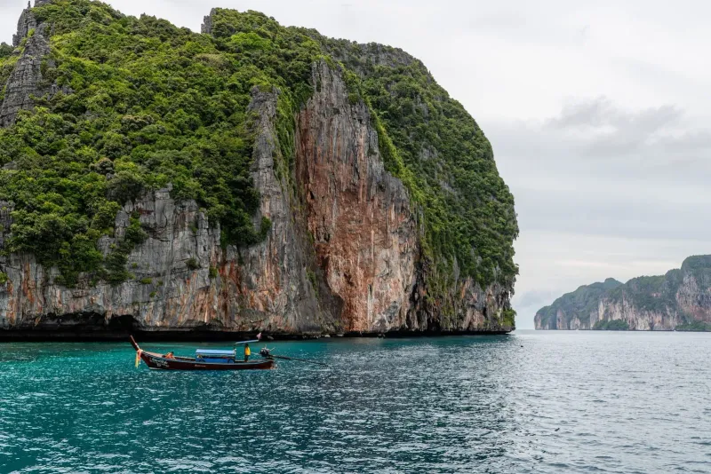 Longtail boat navigating turquoise water beneath limestone cliffs near Phuket Thailand