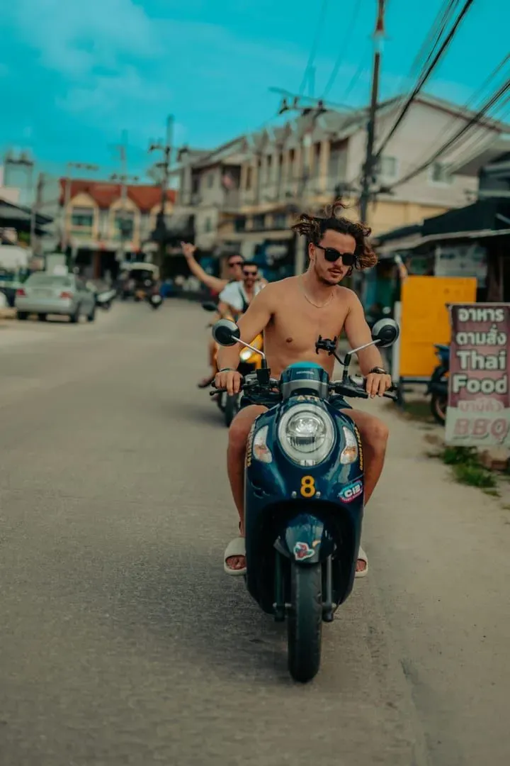 Traveler riding a rental scooter on a sunny Thai street, a common budget transport option on Koh Samui