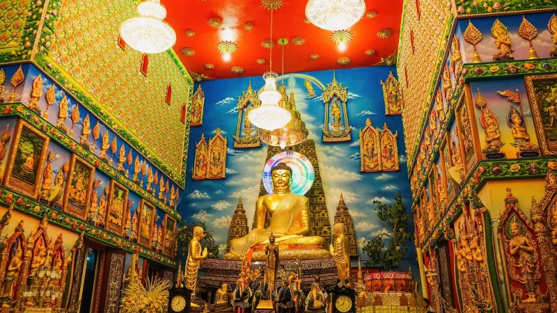 Golden Buddha statue and painted murals inside a Thai ubosot prayer hall, illustrating classic wat interior architecture