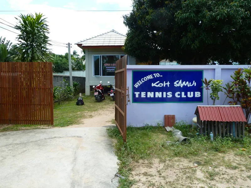 The blue Welcome to Koh Samui Tennis Club sign beside the entrance path
