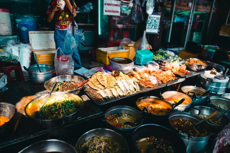 Busy Thai street food market stalls with several cooked dishes on display