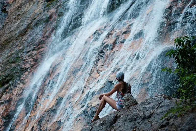 Hiker sitting on rocks beside a cascading waterfall enjoying a Koh Samui viewpoint hike