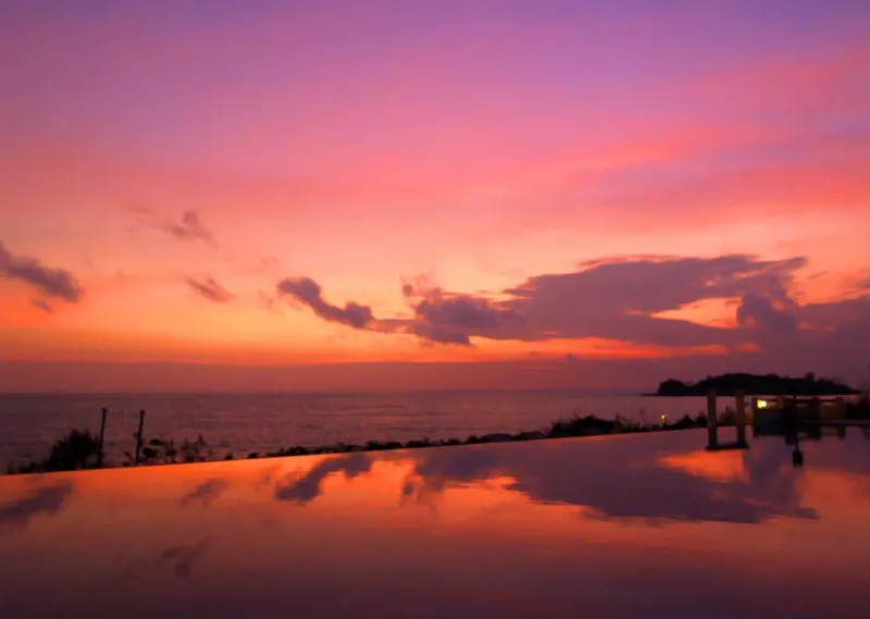 Sunset over the sea with the Laem Yai headland silhouette, seen from a beachfront terrace nearby