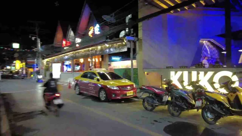 A night street on Koh Samui with a taxi, scooters and neon signs