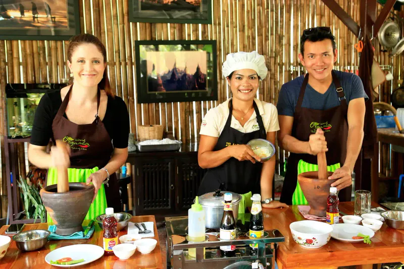 Three people in aprons with a stone mortar at a Thai cooking class table
