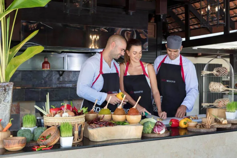Three cooks in dark aprons chopping vegetables at a prep counter
