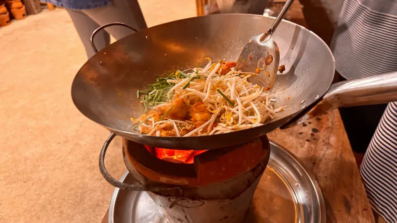 A wok over a charcoal burner with a stir-fried noodle dish