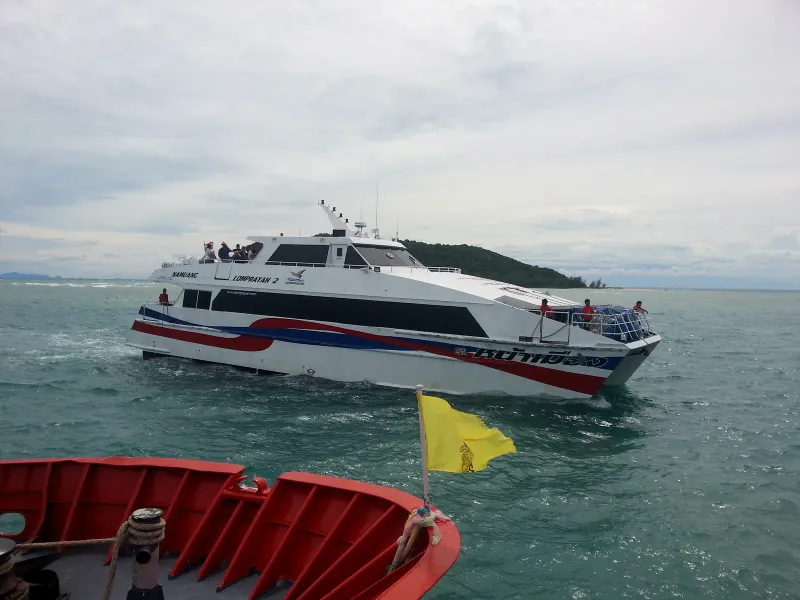 White Lomprayah 2 catamaran with red and blue stripes crossing green water near a forested island