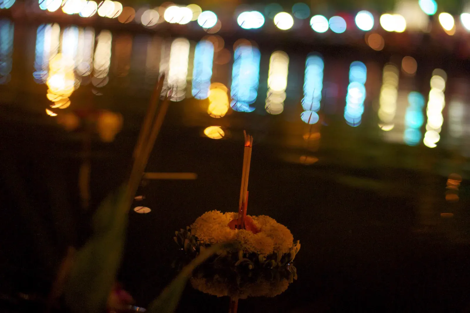 Candle-lit krathong floating on the water at night during Loy Krathong
