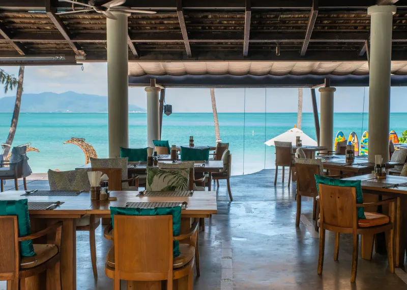 Beachfront restaurant terrace at Melati Beach Resort with turquoise chairs facing the bay