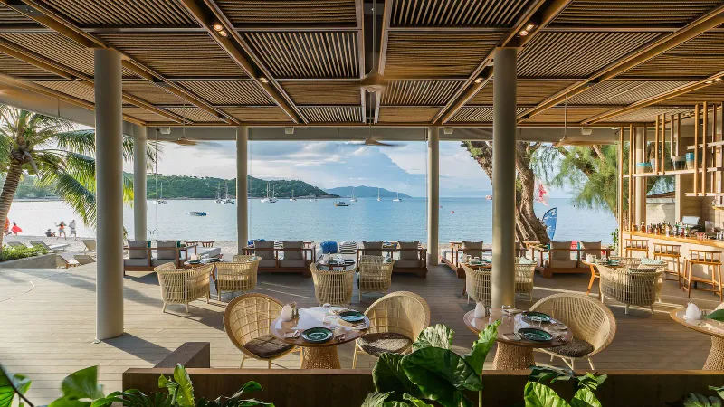 Open-air beachfront restaurant at Melia Koh Samui with rattan chairs and sailboats on the bay