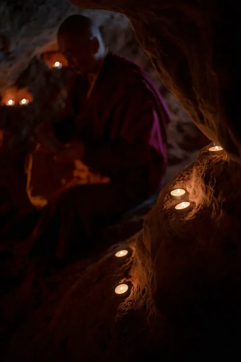 Tea light candles lining a rock ledge inside a dim cave shrine