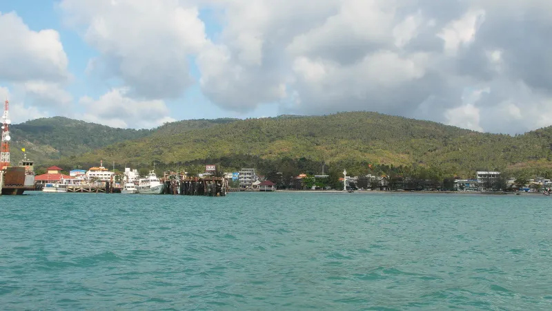 View across the sea to Nathon pier and the town below forested hills on Koh Samui