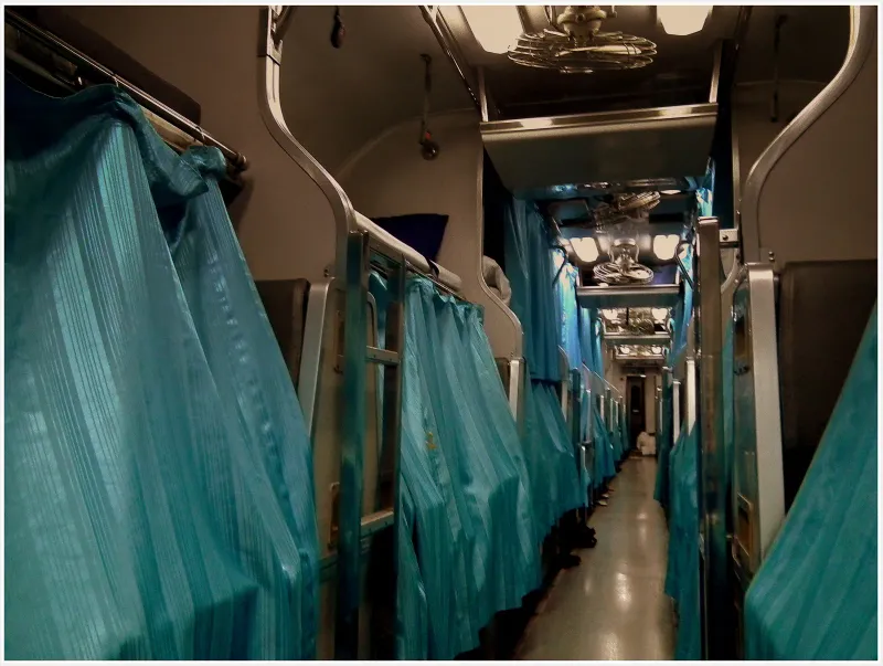 Aisle of a Thai overnight sleeper carriage with teal curtains drawn across the berths