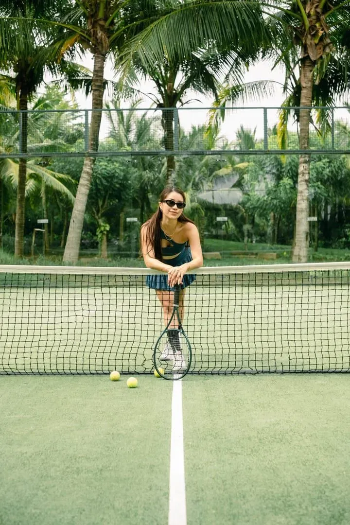 Player leaning on a net on an outdoor court surrounded by palm trees, the Lamai sport scene beyond padel