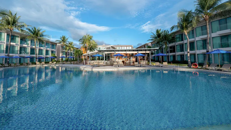 Wide swimming pool at OZO Chaweng Samui with palm trees, blue parasols and the room blocks behind