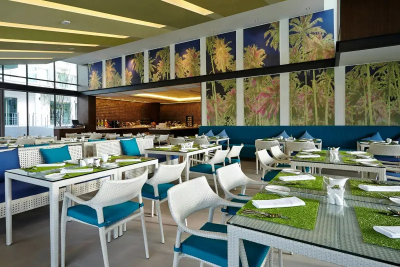 Dining room at OZO Chaweng Samui with white chairs, green table runners and palm-print glass panels