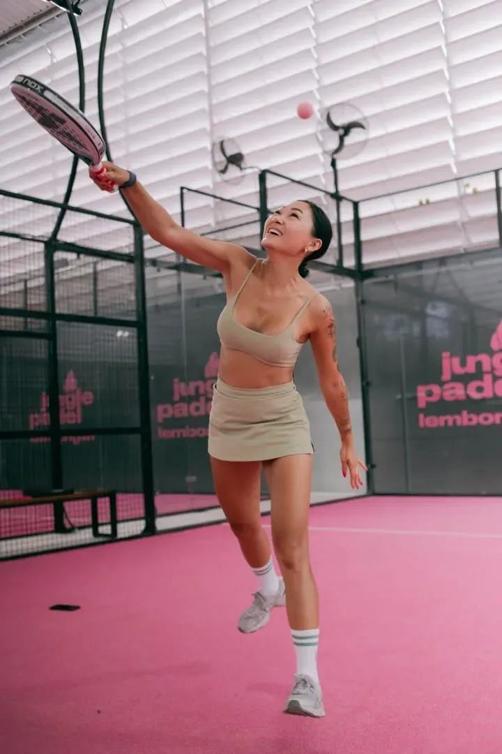 Player reaching for a shot on a pink-toned indoor padel court, the fast rally style a covered court supports