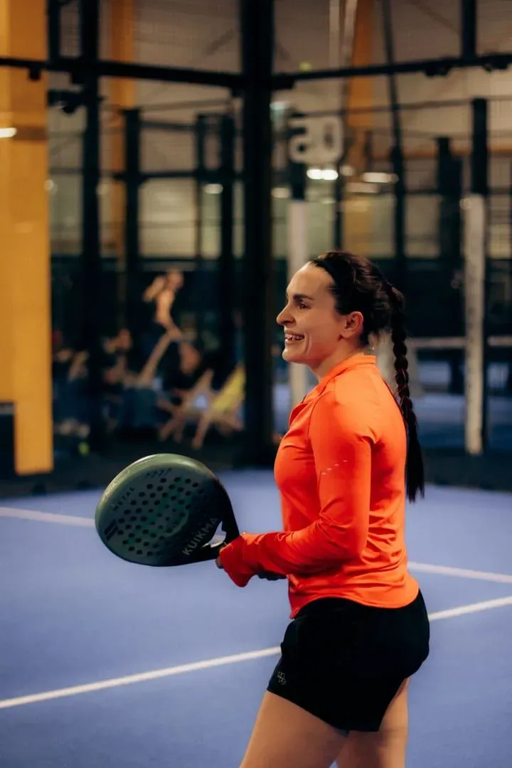 Player holding a padel paddle on a blue-surfaced indoor court between rallies at a Koh Samui padel club