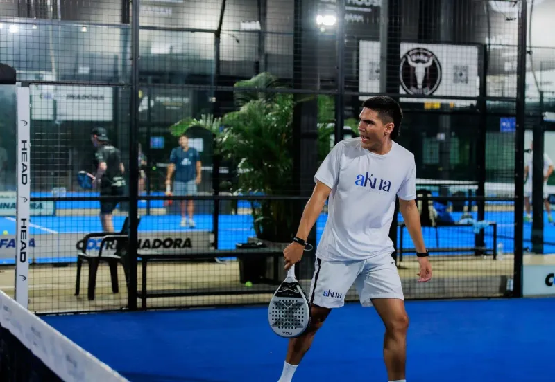 Padel player mid-swing on an indoor court, the fast rally style that fills a covered court on Lamai's main road