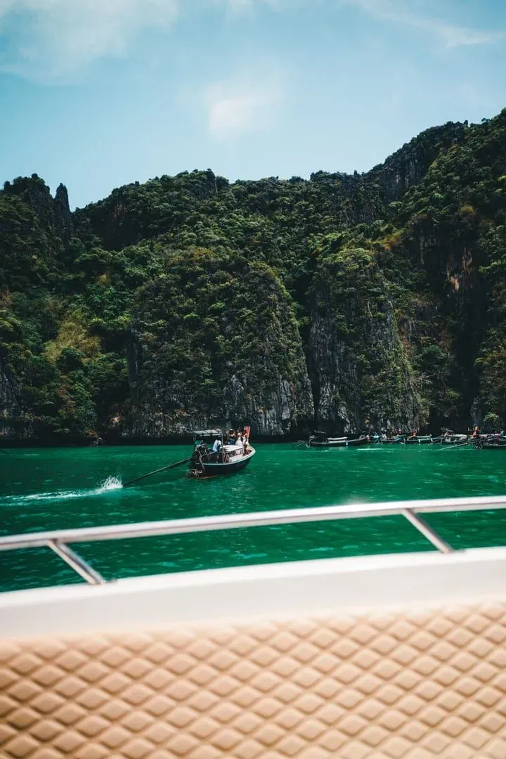 Boat crossing emerald green water beside limestone cliffs on the Andaman coast