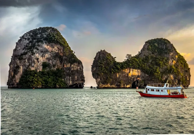 Boat sailing near limestone islands on the Andaman Sea at golden hour