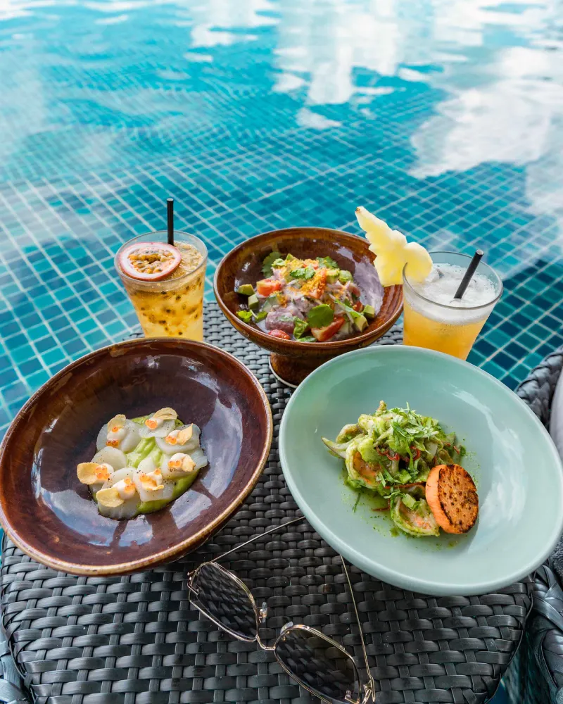 Ceviche, Jakobsmuschel-Crudo und zwei Fruchtcocktails auf einem Tisch am Pool