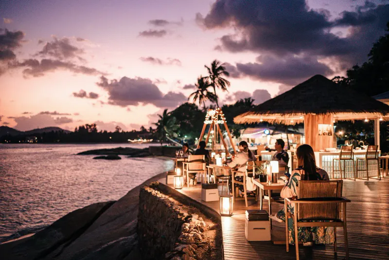 Sunset over the bay with lit beach tables on rocks at Rocky's Boutique Resort in Lamai