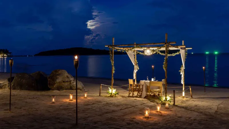 Private beach dining table under a canopy lit by torches at SALA Samui Chaweng at night