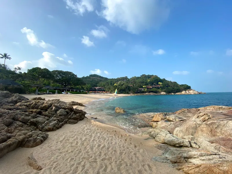 Boulders and a small sandy inlet backed by resort greenery at Thongson Bay's rocky point