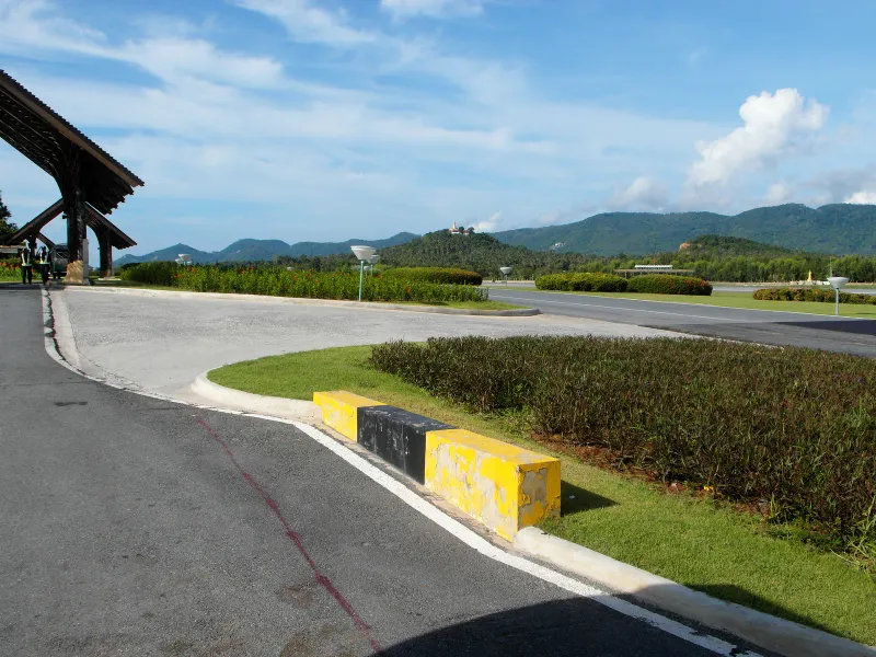 Public road curving away from the Samui Airport entrance, where app drivers pick up passengers