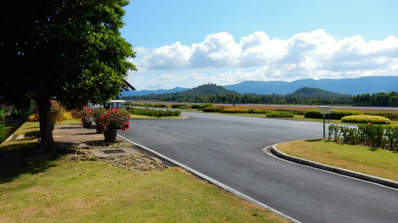緑の丘と、その奥の丘の上の寺院を背にした、サムイ空港の滑走路脇の整備された道