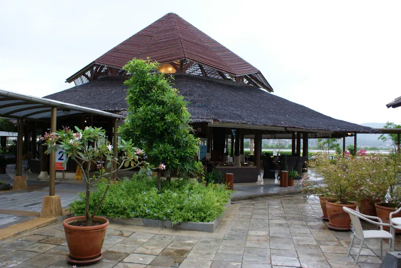 Thatched pavilion roof and frangipani plants at the open-air domestic departures area of Samui airport