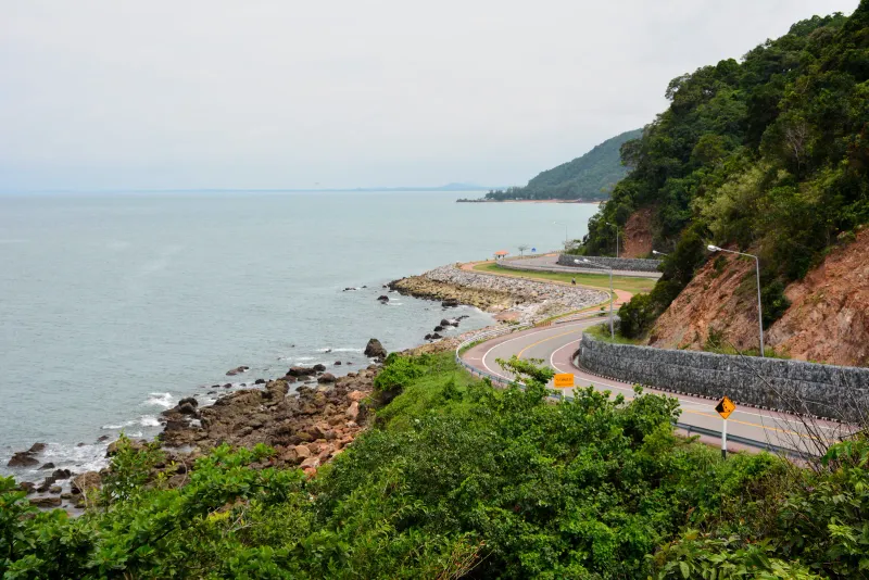 Curving coastal road hugging a forested headland above a calm sea in Thailand