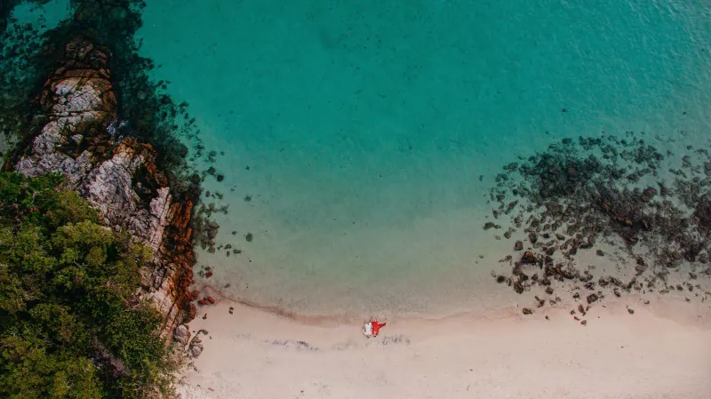 Aerial view of a secluded tropical beach with turquoise water and a coral reef, the kind of quiet cove couples seek out on Koh Samui