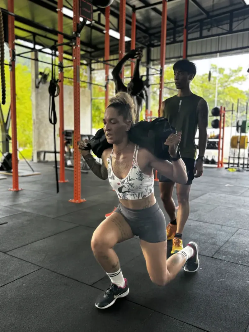 A woman lunging with a weighted bag beside a trainer in a box with orange rig posts