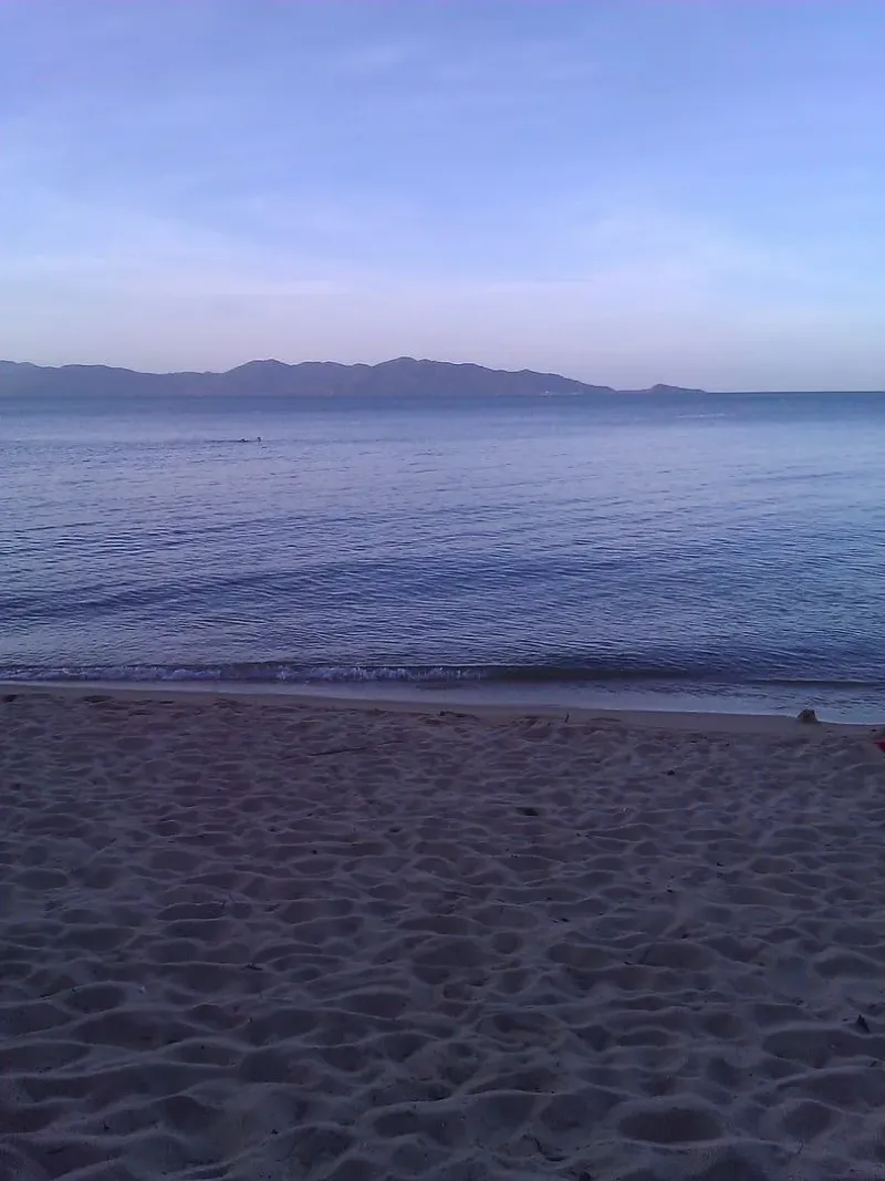 View across calm water from Maenam Beach toward a mountainous island silhouette in the evening light