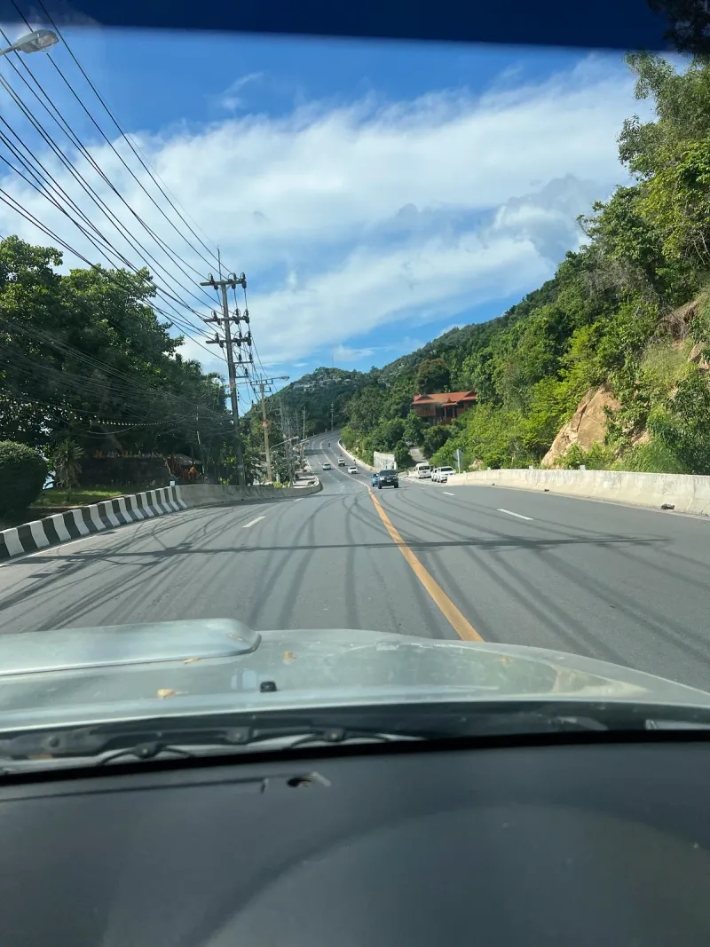 Two lane hill road on a Thai island with cars, a truck and a scooter