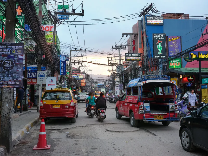Busy Koh Samui street with a red songthaew, taxis, scooters and shop signs