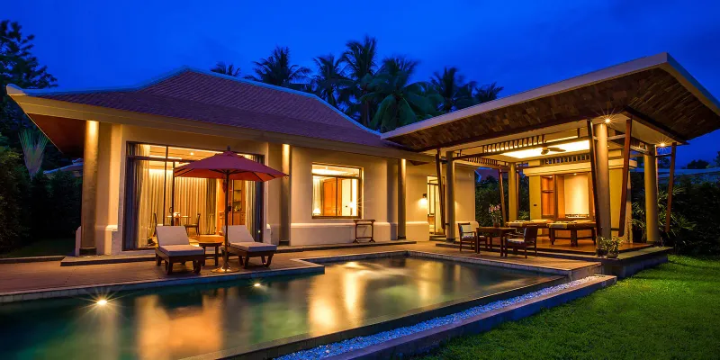 Pool villa glowing at dusk with lit terrace, red umbrella and loungers at Santiburi Koh Samui
