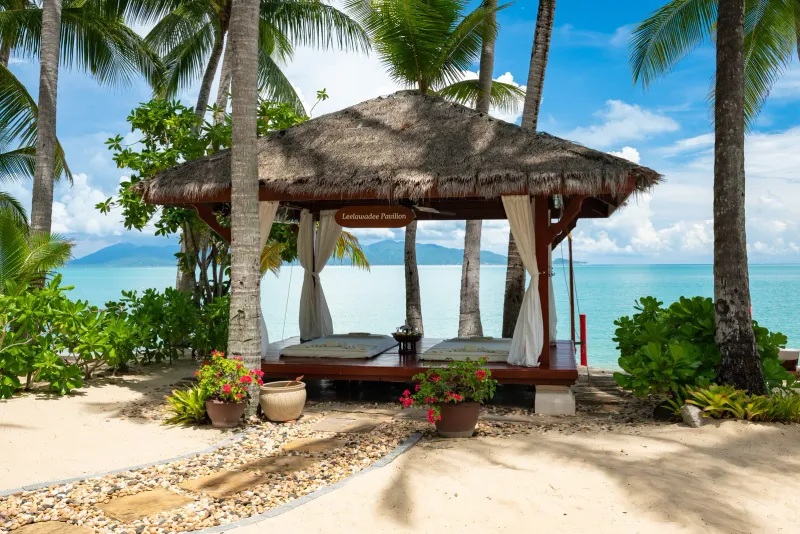 Thatched beachfront massage pavilion with white curtains facing the turquoise bay at Santiburi Koh Samui