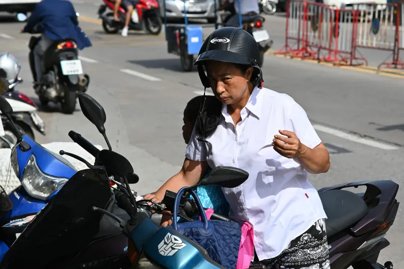 Woman in a black half-face helmet standing beside parked scooters on a Thai street